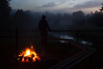 silhouette photo of a person standing near body of water and bonfire