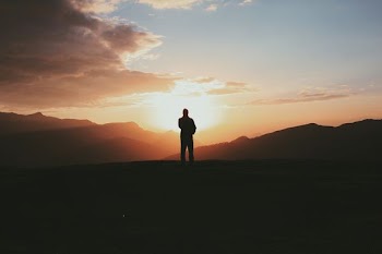 silhouette photo of man standing on mountain during golden hour