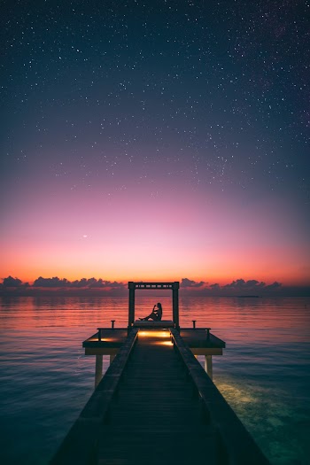 Silhouette Photo of Person Sitting on Boardwalk