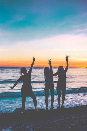 silhouette photo of three women standing near shoreline