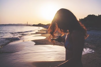 silhouette photo of woman standing on seashore during golden hour