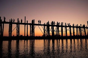 silhouette photograph of two person standing on wooden bridge during golden hour