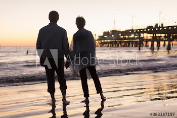 Silhouette senior couple holding hands on beach at sunset