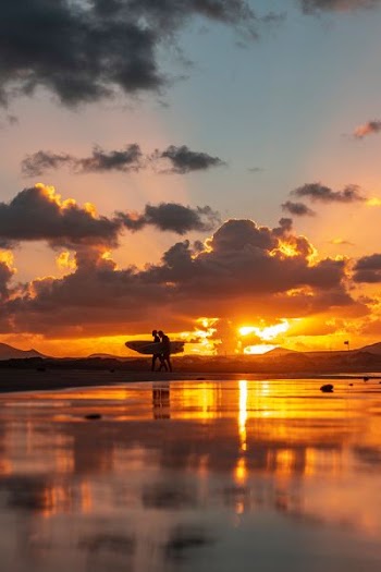 silhoutte photo of two person walking near body of water during sunset