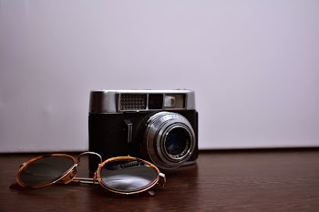 Silver and Black Dslr Camera With Brown Sunglasses on Brown Wooden Surface