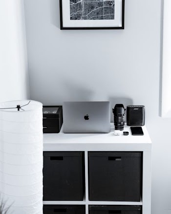 silver MacBook beside black camera lens and speaker on dresser