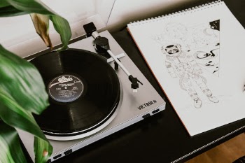 Silver sophisticated Victrola record player on a desk next to a beautiful hand drawing of an astronaut. 
