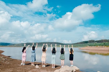 Six Girls Raise Their Hands in Front of Body of Water