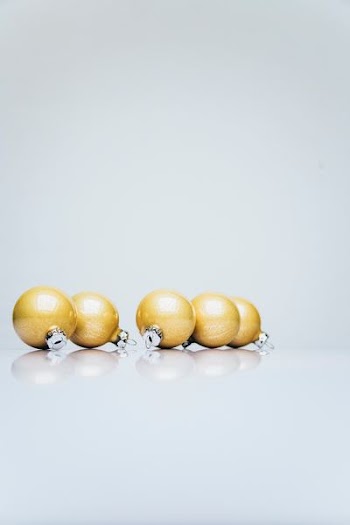 six gold Christmas baubles on white wooden surface