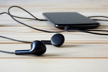Smartphone And Black Earphones On Wooden Surface