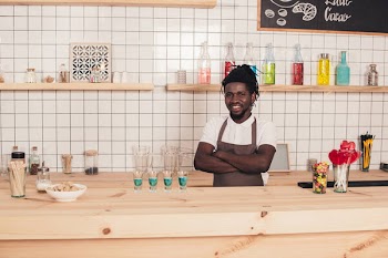 Smiling african american bartender with blue cocktails in shot glasses at bar counter