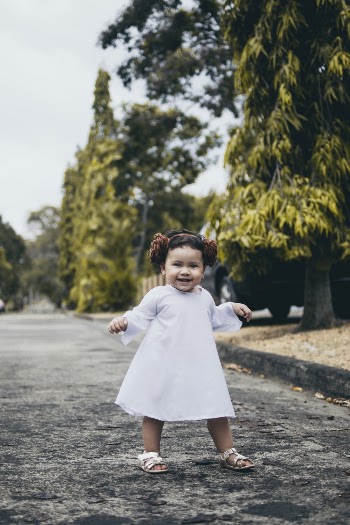Smiling Baby Girl Wearing White Dress Standing on Road