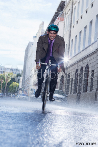 Smiling businessman riding bicycle on rainy city street