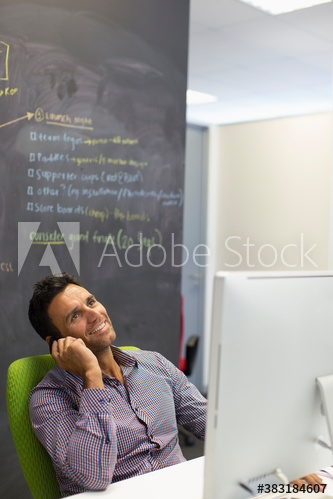 Smiling businessman talking on smart phone at computer
