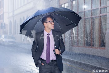 Smiling businessman with umbrella on rainy city street