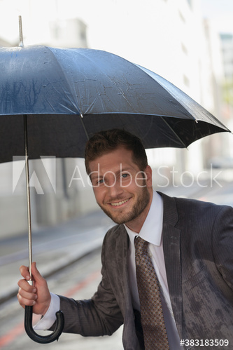 Smiling businessman with umbrella on rainy street