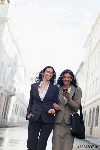 Smiling businesswoman with smart phone walking on city street