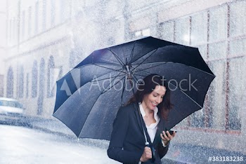 Smiling businesswoman with umbrella and smart phone on rainy street