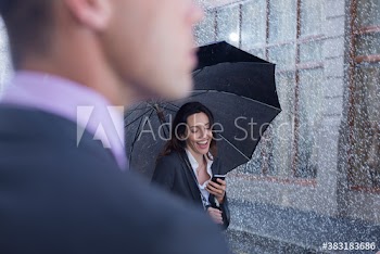 Smiling businesswoman with umbrella and smart phone on rainy street