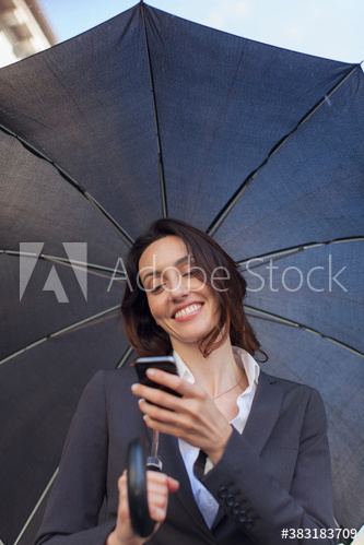 Smiling businesswoman with umbrella using smart phone