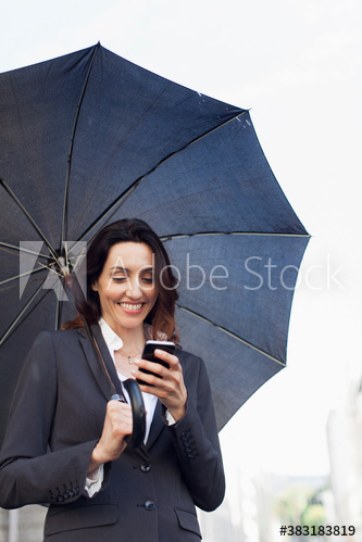 Smiling businesswoman with umbrella using smart phone