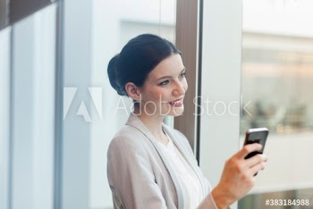 Smiling corporate businesswoman using smart phone in office window