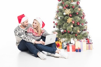 Smiling couple in santa claus hats with laptop near christmas tree isolated on white