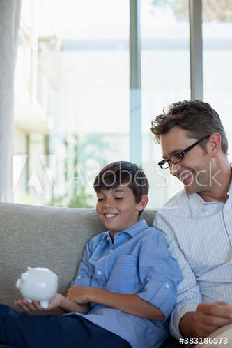 Smiling father and son with piggybank on sofa