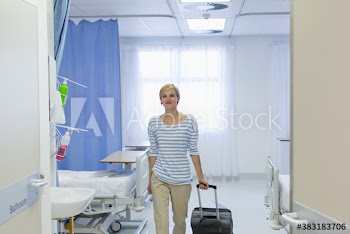 Smiling female patient with suitcase leaving hospital room