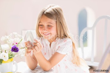Smiling girl using smart phone at sunny table with flowers