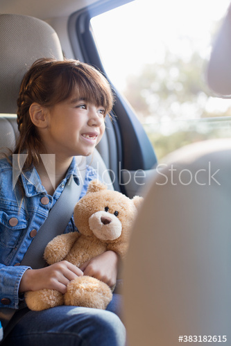 Smiling girl with teddy bear riding in backseat of car
