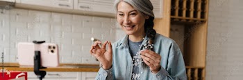 Smiling grey woman showing costume jewelry while taking selfie footage