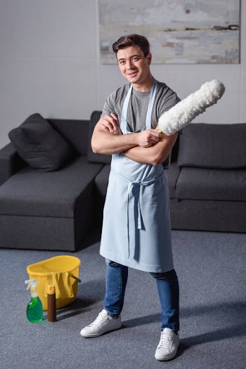 Smiling handsome man standing and holding brush for cleaning dust in living room