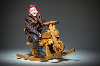 Smiling kid biker sitting on wooden rocking motorbike on grey...