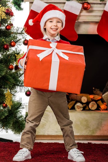 Smiling little kid holding big red christmas gift and looking at camera