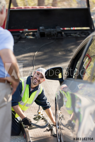 Smiling male roadside assistance mechanic preparing to tow car