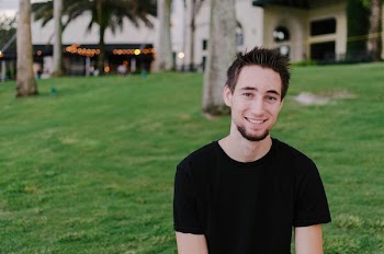 smiling man in black shirt standing near trees