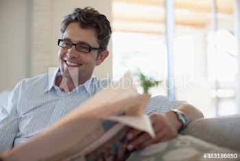 Smiling man reading newspaper on sofa