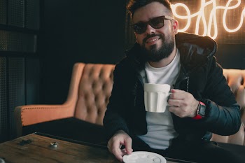 Smiling Man Sitting Near Table Holding Ceramic Mug Inside Room