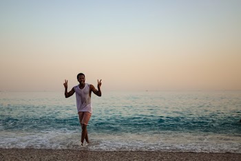 Smiling Man Wearing White Tank Top Walking at Seashore