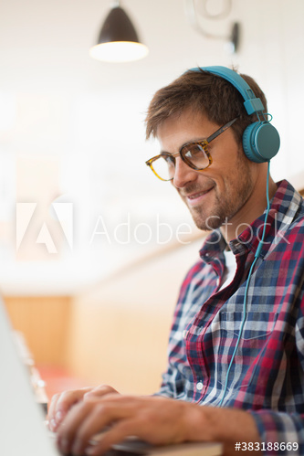 Smiling man with headphones working at laptop in cafe