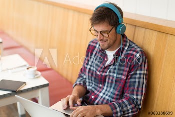 Smiling man with headphones working at laptop in cafe