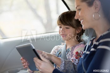 Smiling mother and daughter using digital tablet in backseat of car
