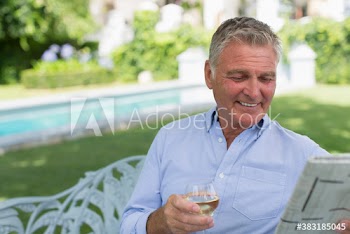 Smiling senior man drinking wine and reading newspaper in garden
