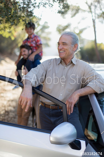 Smiling senior man leaning against car at roadside