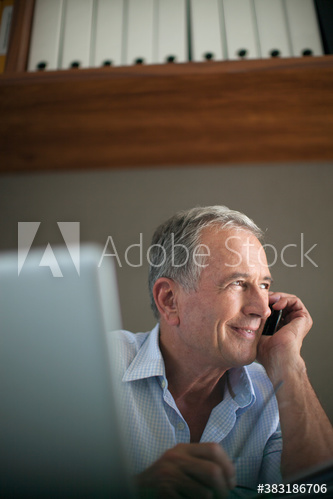 Smiling senior man talking on smart phone at laptop
