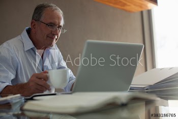 Smiling senior man with coffee working at laptop