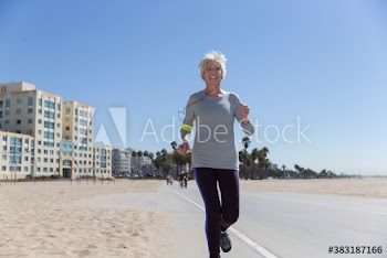 Smiling senior woman jogging on sunny beach boardwalk