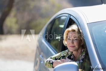 Smiling senior woman leaning out sunny car window