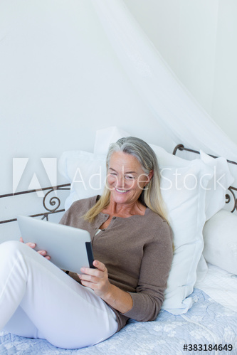 Smiling senior woman relaxing with digital tablet on daybed